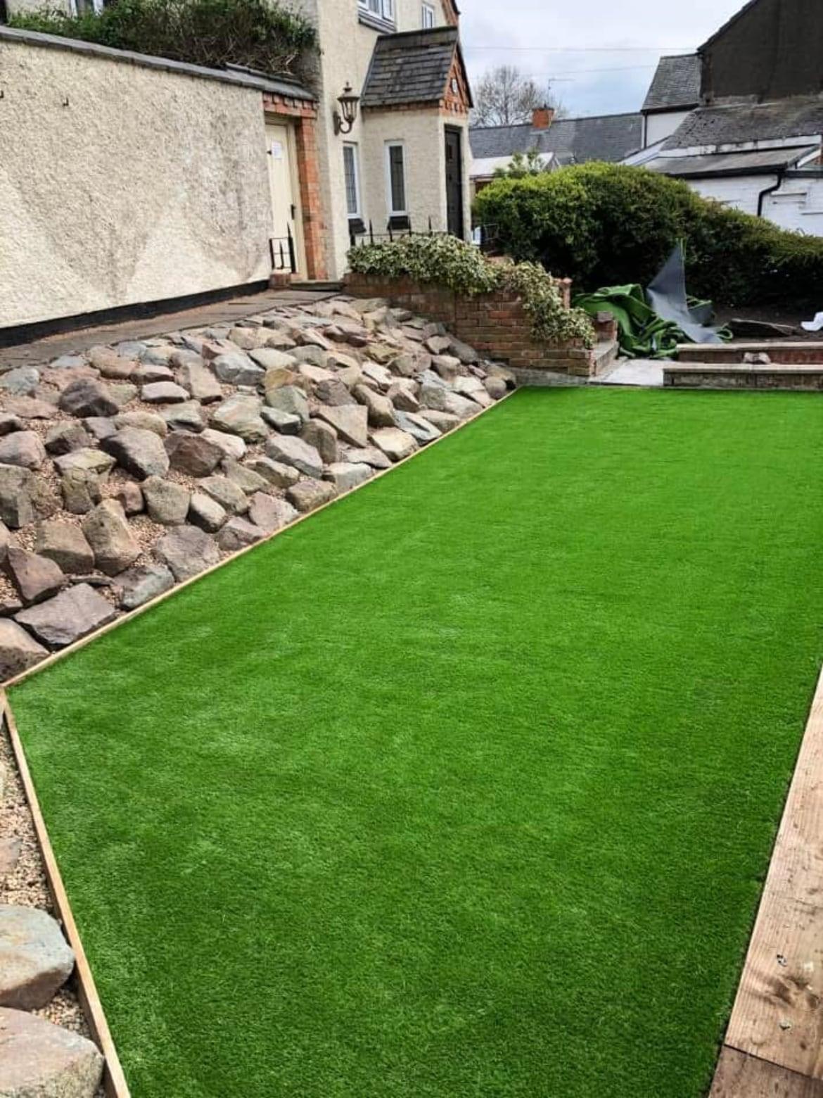 Artificial lawn running alongside a sloping rockery bank of natural stone