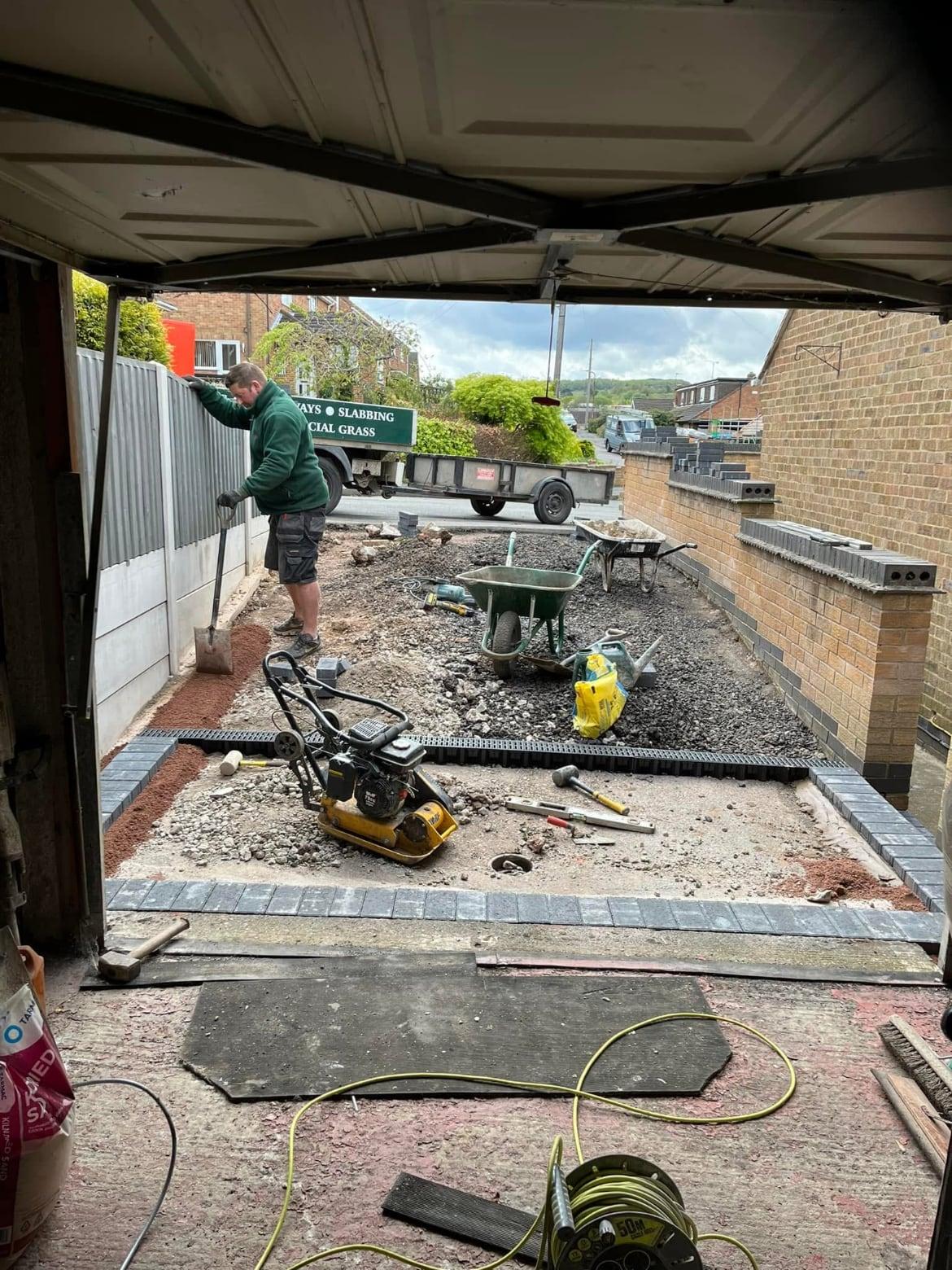 Driveway sub-base being compacted with a plate compactor, viewed from inside the garage