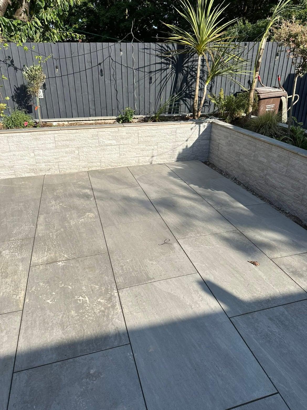 Grey porcelain patio with stone-effect raised beds against a dark painted fence
