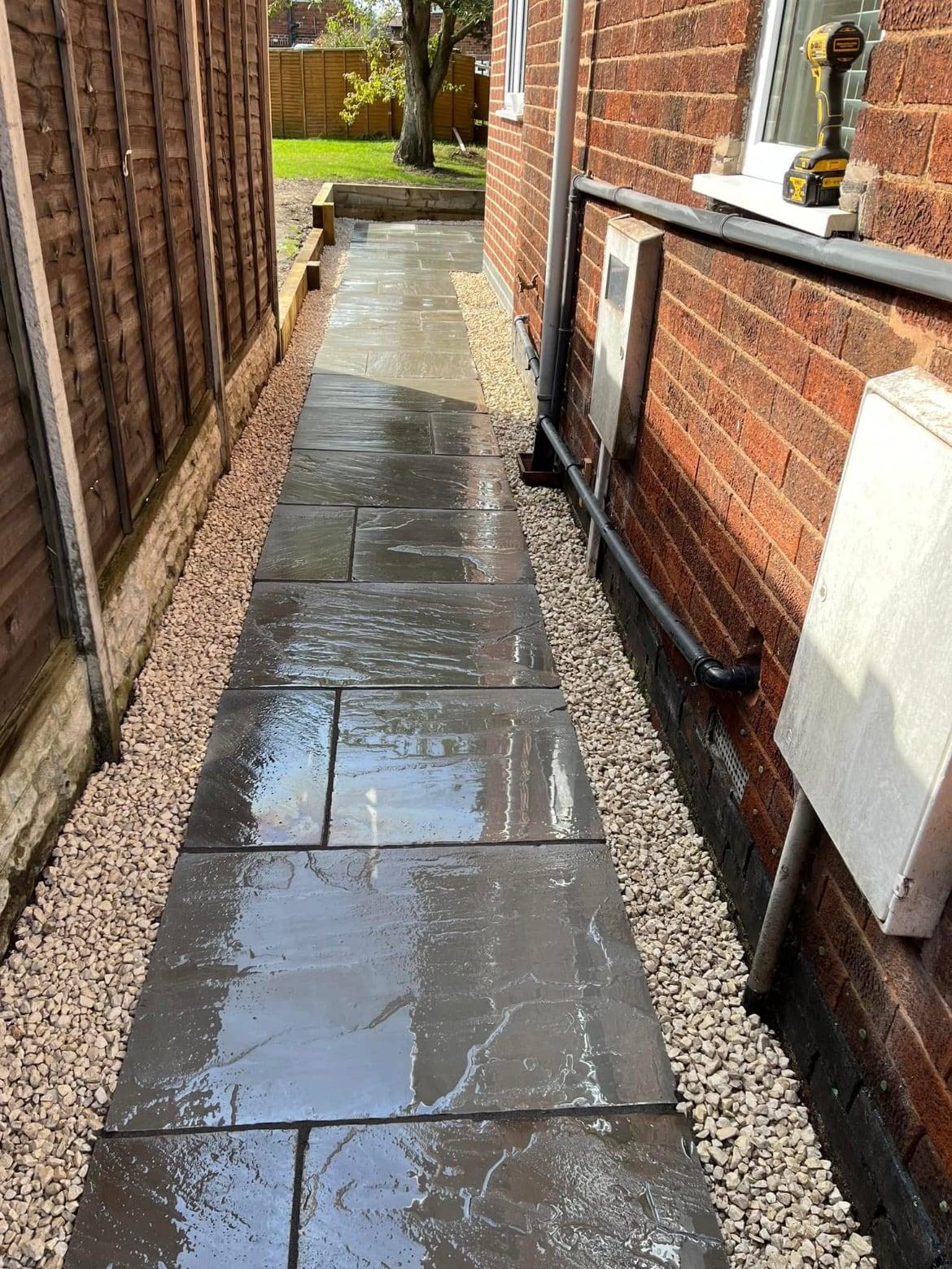 Narrow side return paved in grey sandstone with gravel either side, running along a brick house