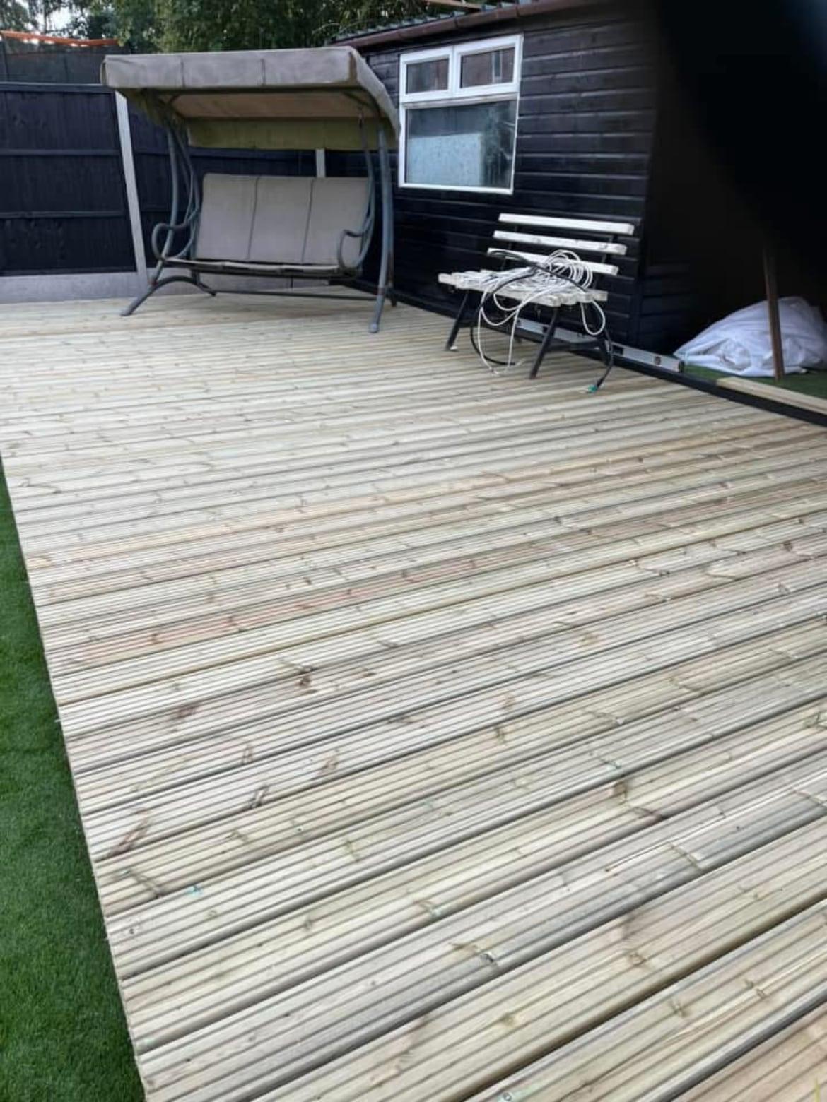 New timber decking with a garden swing seat in front of a dark painted outbuilding
