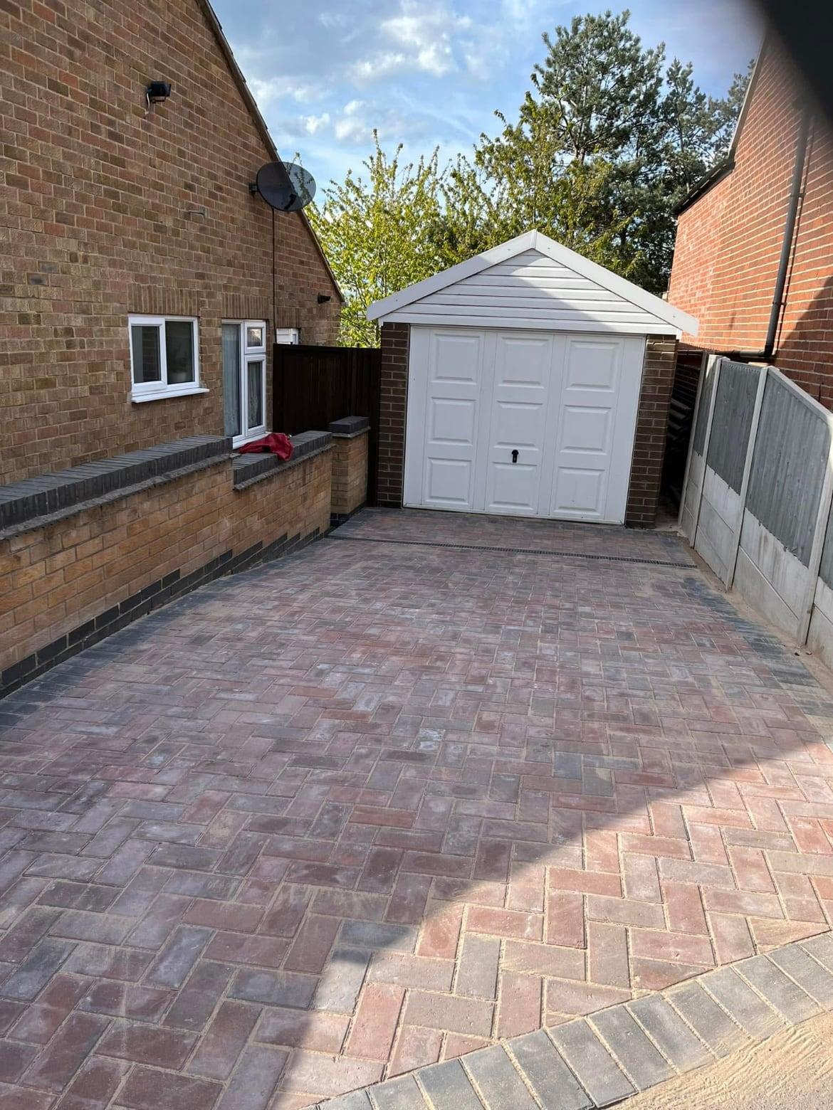 Red herringbone block-paved driveway with charcoal edging leading to a white garage door